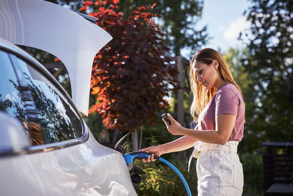 woman charging an electric vehicle while looking at her phone