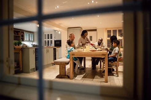 Looking in through a window at people gathered for a meal
