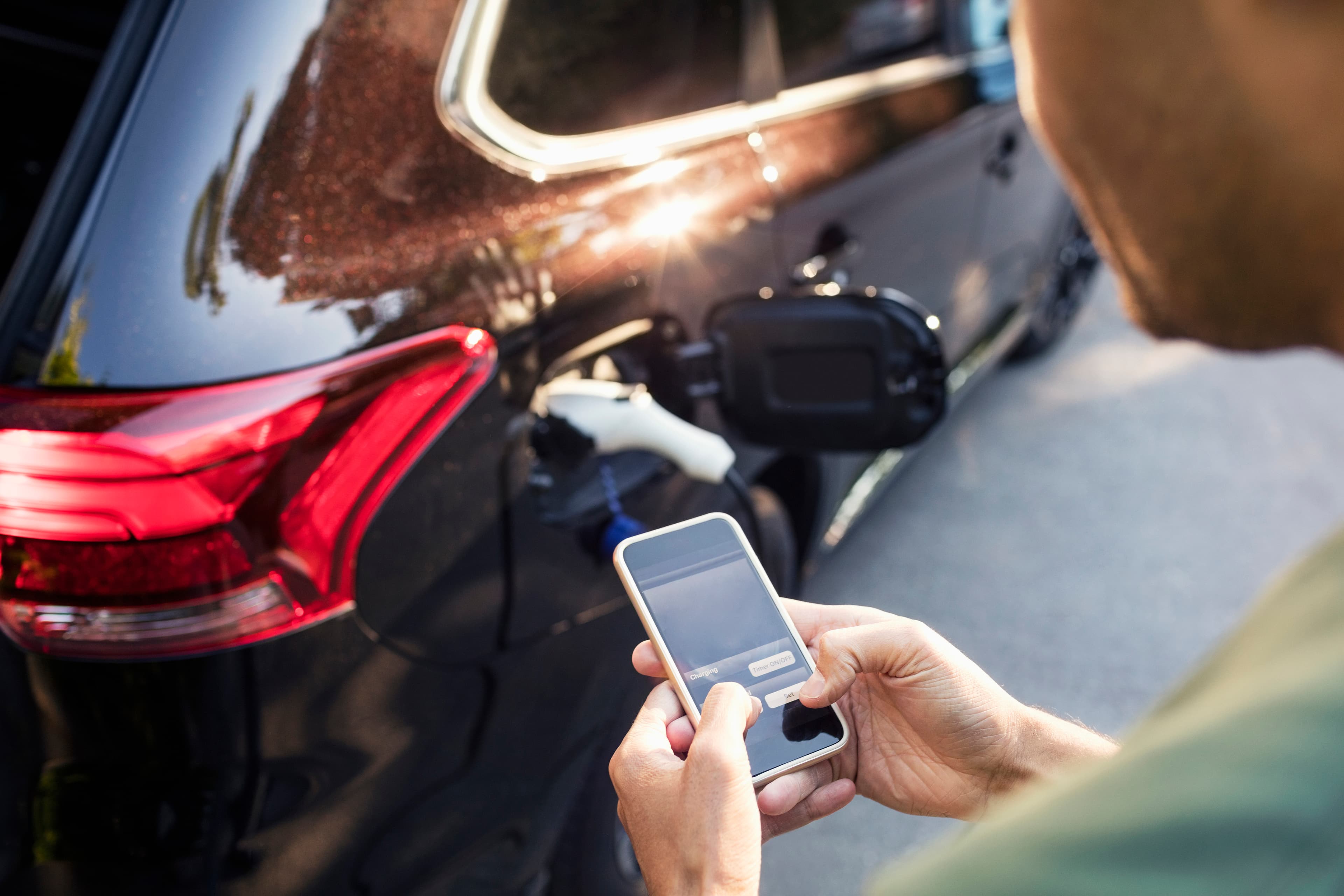 Man standing next to electric vehicle checking his mobile phone