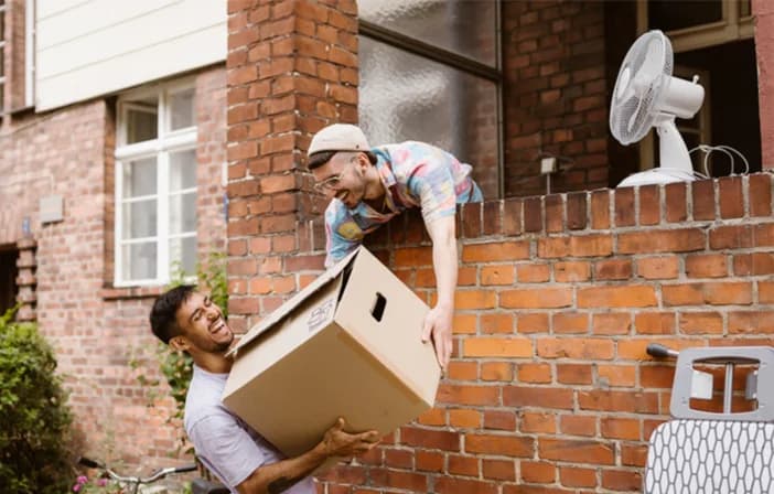 gay couple passing box over balcony while moving house