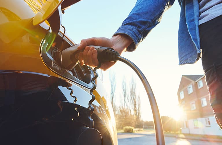 close up of person standing next to their electric vehicle, charging their car
